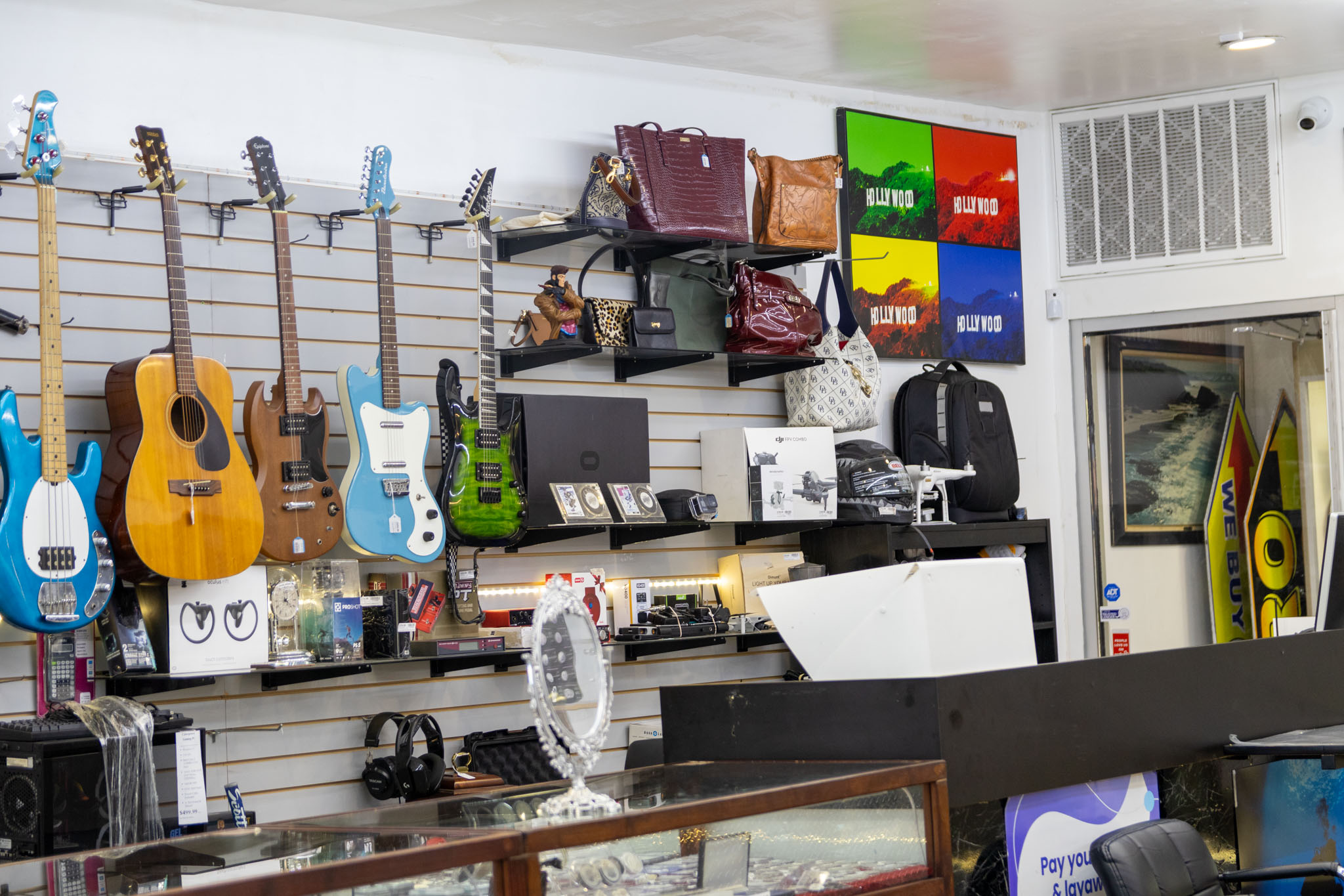 The image shows a wall full of various items, such as guitars, smaller electronics, and high-end designer bags.